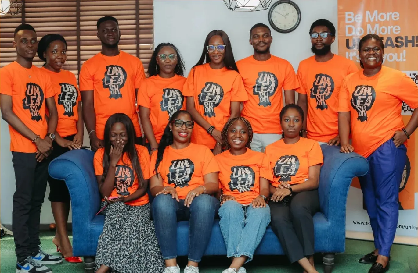 The 2024 UNLEASH Leaders Envoys in orange UNLEASH t-shirts, gathered around a blue sofa
